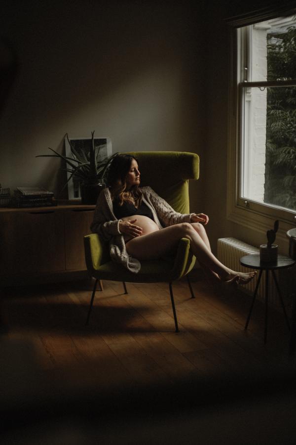 Femme enceinte assise dans un fauteuil pendant une séance grossesse à la maison