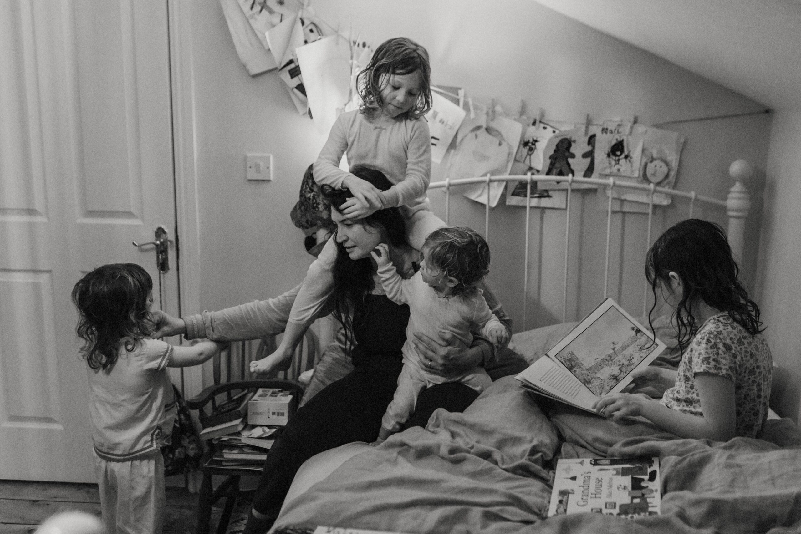 Maman assise sur un lit préparant ses filles à aller se coucher pendant une séance photo motherhood
